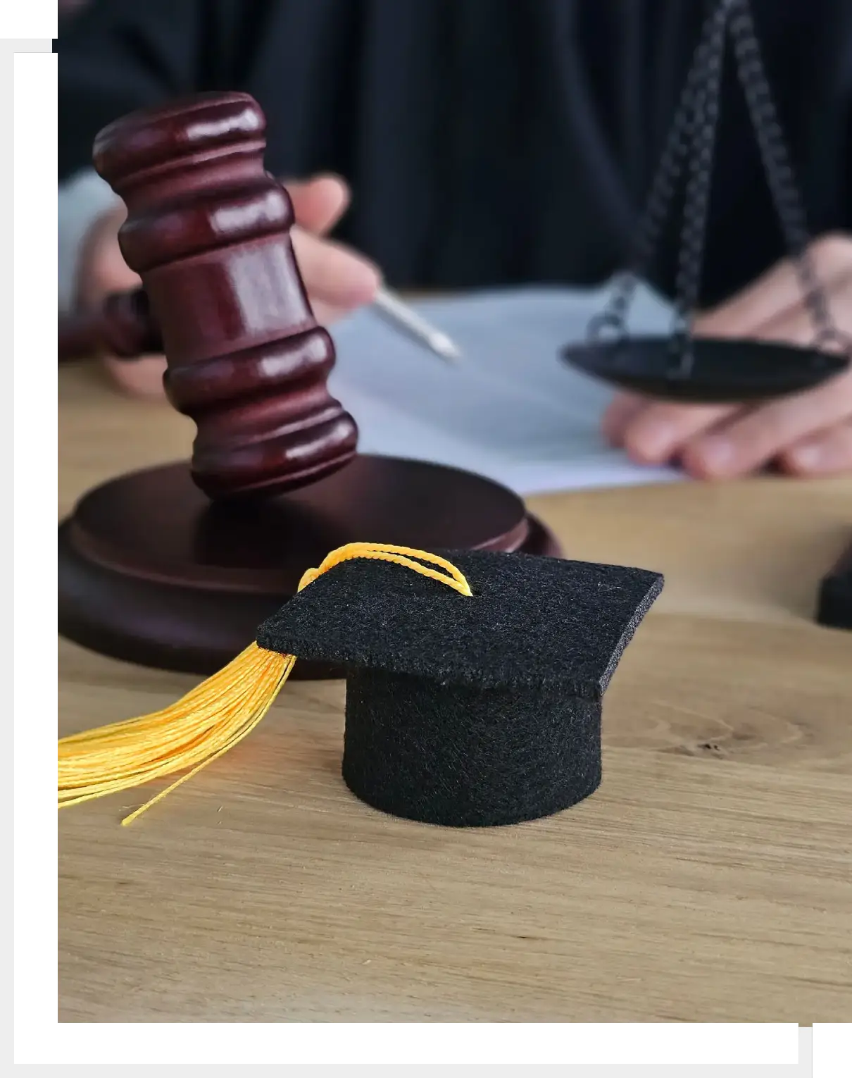 A judge's gavel and a miniature graduation cap on a wooden table.