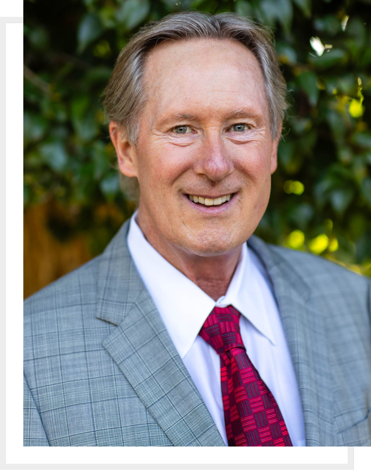 Smiling man in a gray suit and red tie outdoors.