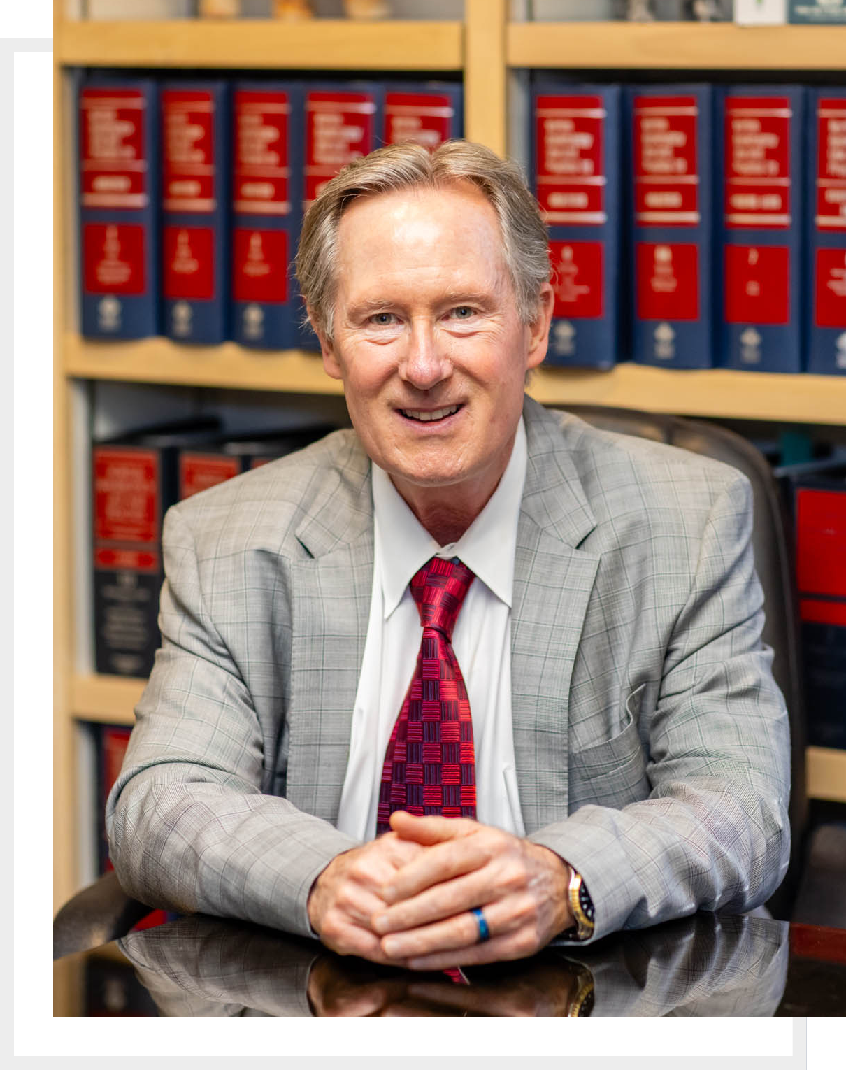 A man in a gray suit sitting at a desk with law books behind him.